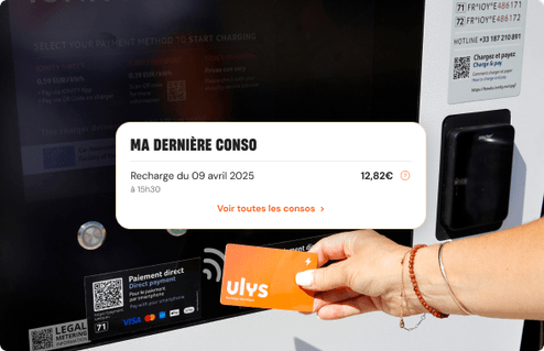 Main tenant une carte de service devant une borne de recharge affichant des informations de consommation.