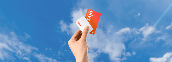 Main tenant une carte de service et un badge télépéage levés vers un ciel bleu avec des nuages.