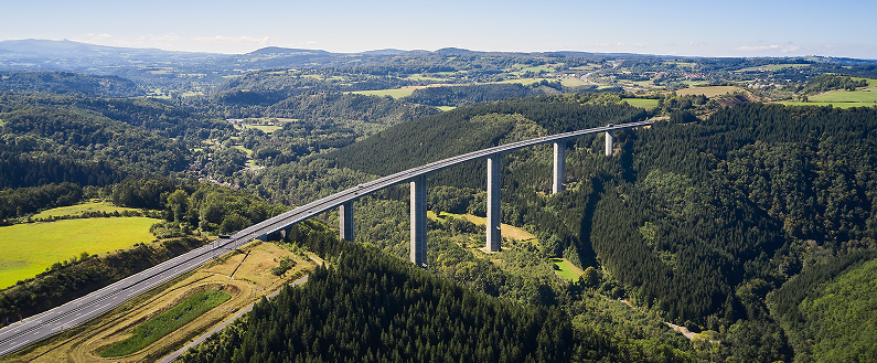 Viaduc autoroutier traversant une vallée boisée, vu en hauteur au‑dessus d’un paysage verdoyant.
