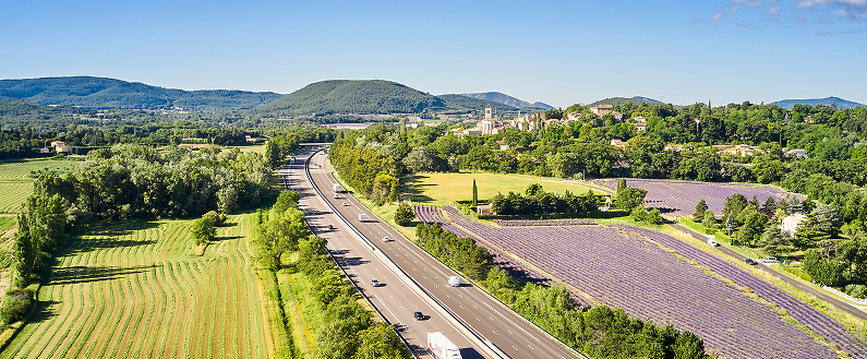 Autoroute traversant des champs et des paysages verdoyants, vue aérienne sous un ciel bleu.