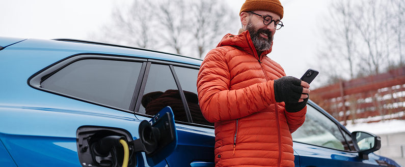Personne utilisant un smartphone à côté d’une voiture bleue en cours de recharge électrique.