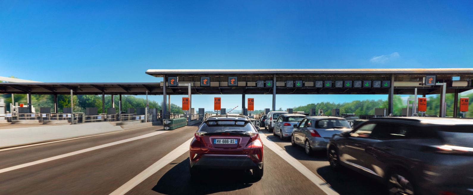 Barrière de péage sur autoroute avec plusieurs véhicules en circulation sous un ciel bleu.