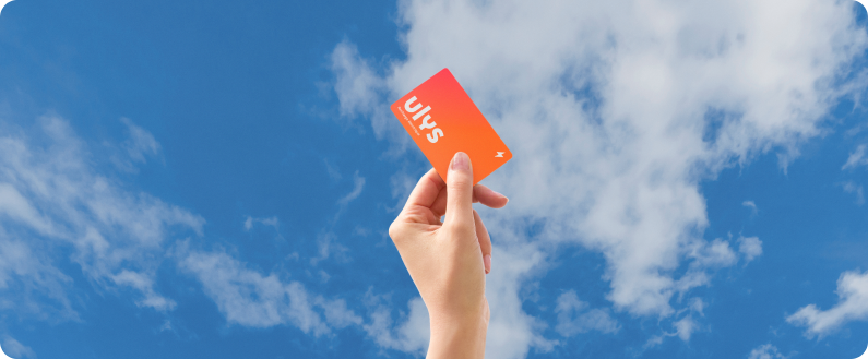 Main tenant une carte orange levée vers un ciel bleu avec des nuages.
