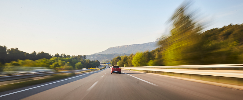 Voiture roulant sur une autoroute entourée de végétation, vue arrière avec effet de mouvement.