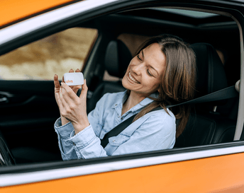 Personne assise dans une voiture tenant un pass télépéage entre ses mains, vue depuis l’extérieur par la fenêtre.