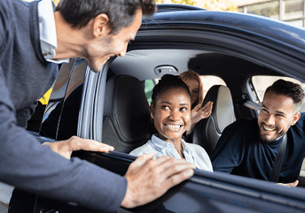 Personnes à l’intérieur d’une voiture, avec une personne à l’extérieur parlant aux passagers par la fenêtre ouverte.
