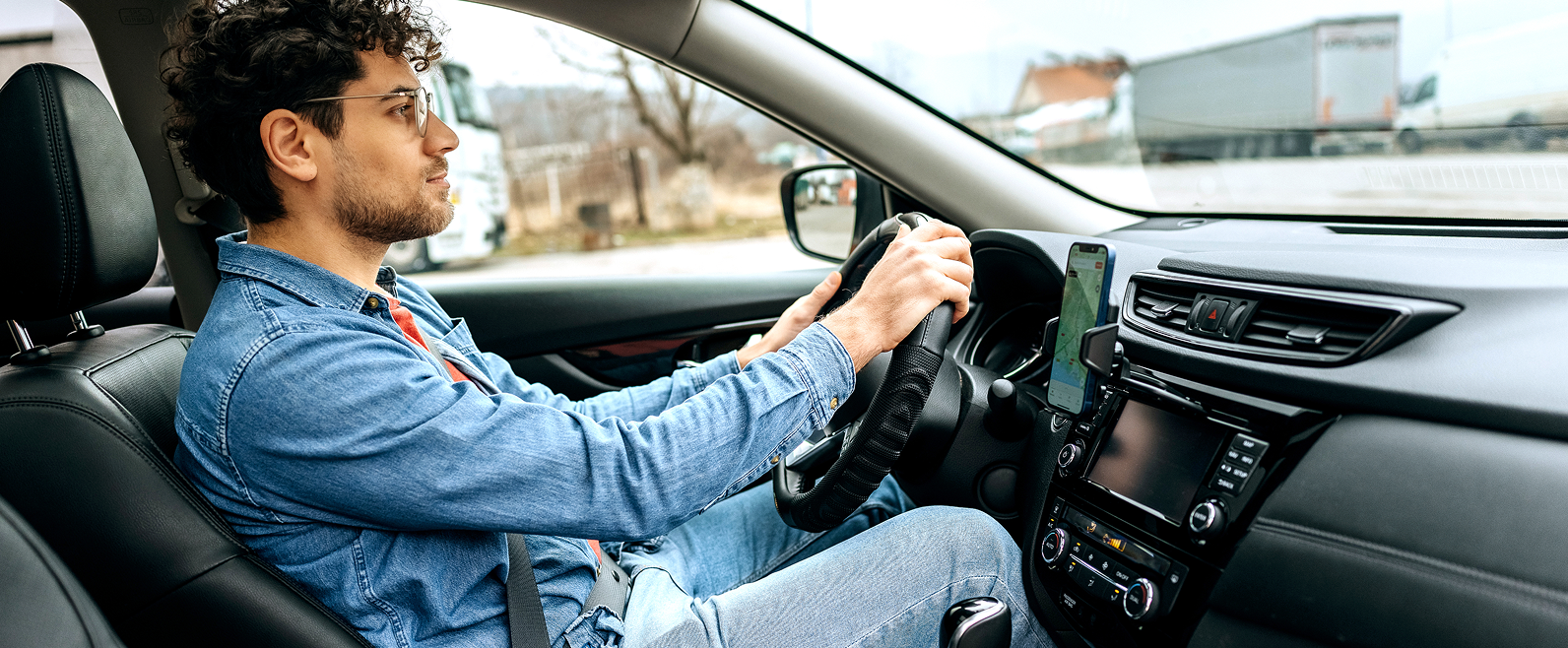 Personne au volant d’une voiture, vue intérieure, avec un smartphone fixé au tableau de bord.