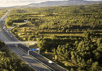 Autoroute traversant un paysage boisé et verdoyant, vue aérienne avec un échangeur et des véhicules en circulation.