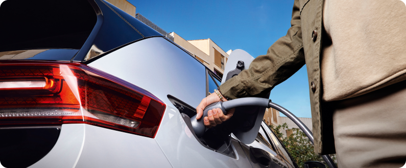 Main branchant un câble de recharge sur une voiture électrique blanche en extérieur.